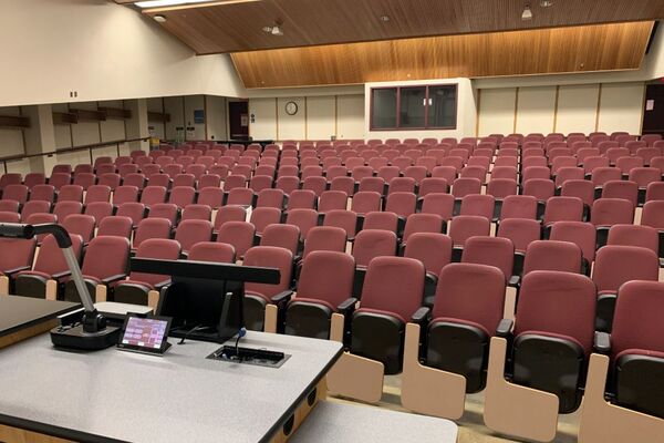 Back of room view of student auditorium seating, A/V booth center, and exit door at left and right rear of room