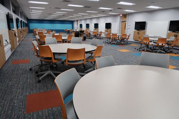 Back of room view of student collaborative table and chair seating and exit door at center right of room