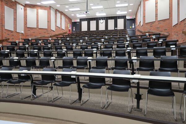 Back of room view of student tiered fixed table and chair seating and exit doors at left and right rear of room