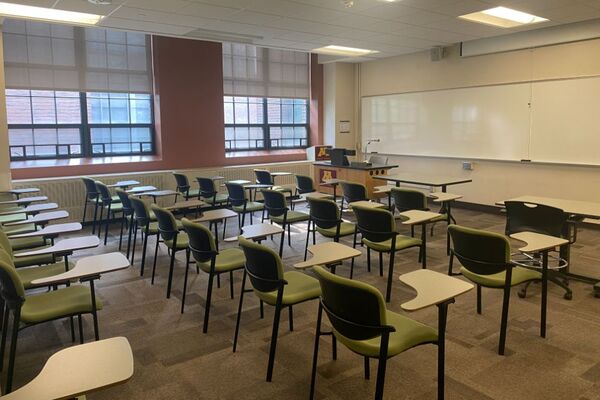 Front of room view with lectern on left in front of markerboard and projection screen raised