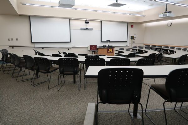 Front of room view with lectern center in front of markerboard and projection screens on left and right lowered