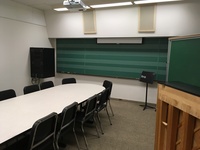 Photo of front of room from back of room with music staff chalkboard and piano.