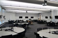 Room view with lectern in center of room, multiple markerboards and student display monitors on all walls, exit door in corner of room