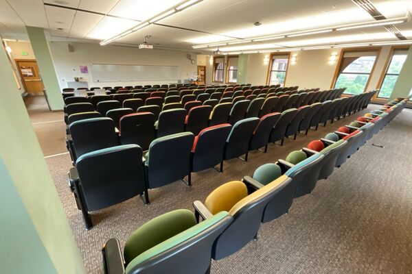 Front of room view with lectern on right in front of markerboard and exit doors on left and right