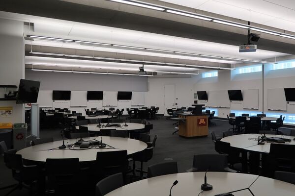 Room view of student active learning round table and chair seating, multiple markerboards and student display monitors on all walls