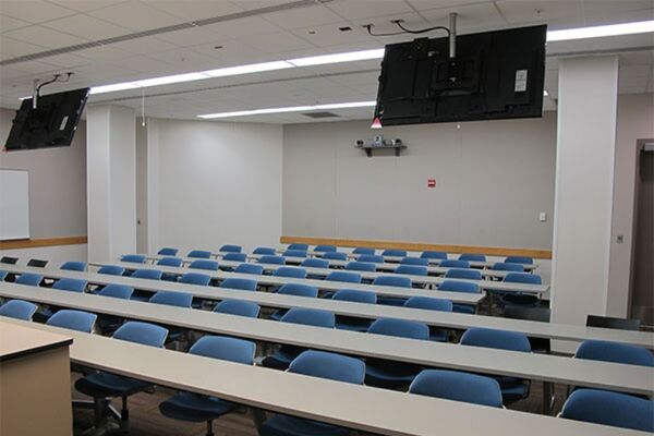TBack of room view of student fixed table and chair seating and exit doors at rear of room