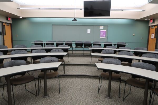 Back of room view of student tiered fixed-table and chair seating and exit doors at rear left and right of room