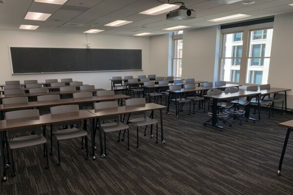 Back of room view of student table and chair seating and chalkboard on rear wall
