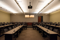 View from front middle of classroom looking towards audience showing projector, rear exit door, instructor camera, rear self view monitors, and audience seating