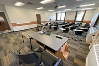 Back of room view of student tablet arm seating, side markerboards on left wall, and exit door center left of room