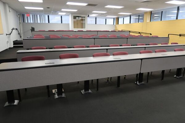 Back of room view of student fixed-table and chair seating and exit door at left rear of room