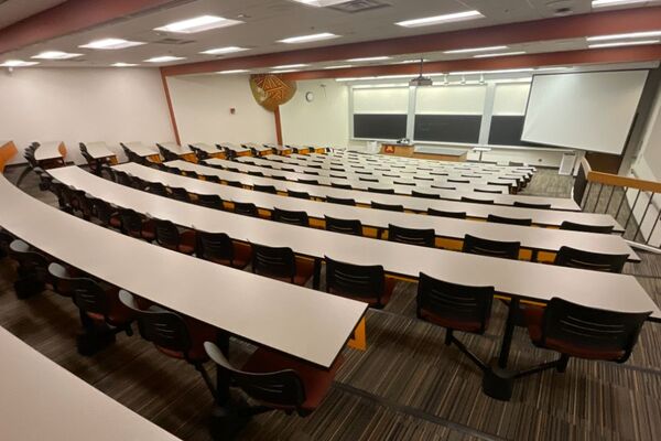 Front of room view with lectern center in front of chalkboards and projection screen lowered on the right