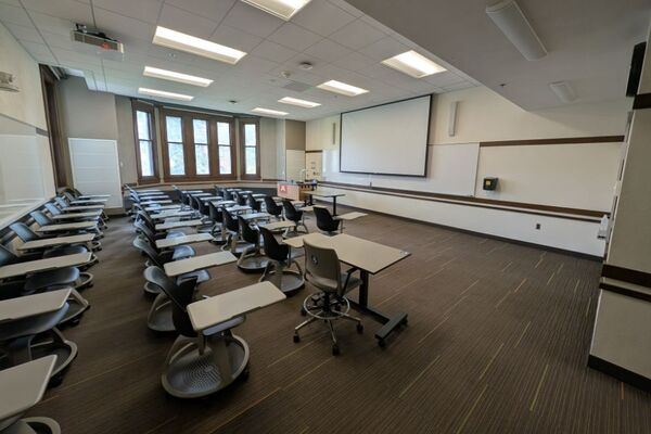 Front of room view with lectern on left in front of markerboard and projection screen partially lowered
