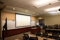 View from Audience left side of classroom showing center projector display, audience cameras, instructor podium and class member seats