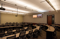 View from audience left side perspective looking towards rear of classroom showing rear exit door, instructor camera, rear self view monitors, and audience seating