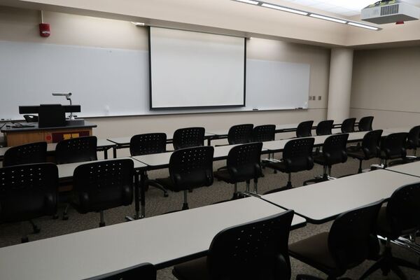 Front of room view with lectern on left in front of markerboard and projection screen lowered