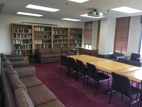 Photo of back of room from front of room, windows on the right wall, conference room table in the middle, and couches along the perimeter.