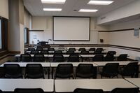Front of room view with lectern on left in front of markerboard and projection screen partially lowered