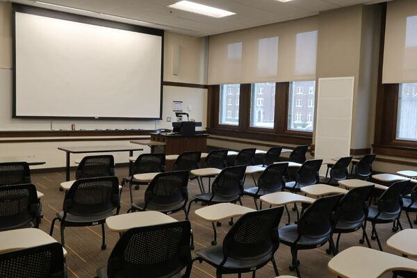 Front of room view with lectern on right in front of markerboard and projection screen partially lowered
