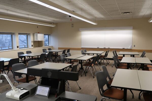 Back of room view of student table and chair seating and markerboard on rear wall