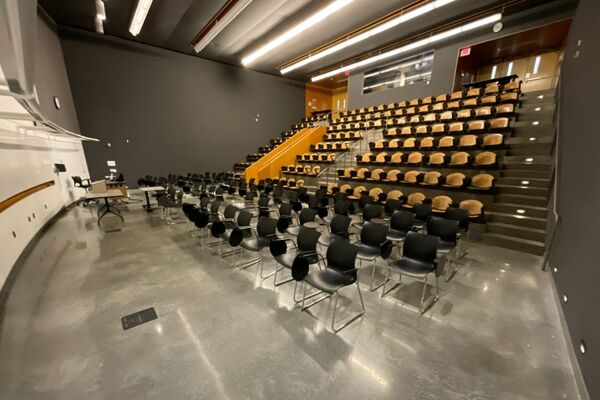 Back of room view of student tablet arm (front) and auditorium seating (rear) and double exit doors at rear of room