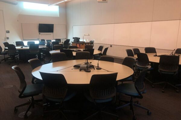 View with lectern on left in front of markerboard, collaborative student seating with round tables and chairs