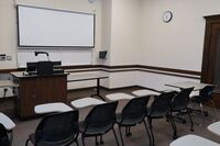 Front of room view with lectern on left in front of markerboard and projection screen partially lowered