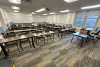 Back of room view of student table and chair seating, and markerboards on rear wall of room